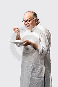 Expressive Indian Old man eating food from empty or blank white plate or bowl