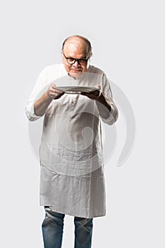 Expressive Indian Old man eating food from empty or blank white plate or bowl