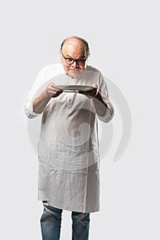 Expressive Indian Old man eating food from empty or blank white plate or bowl