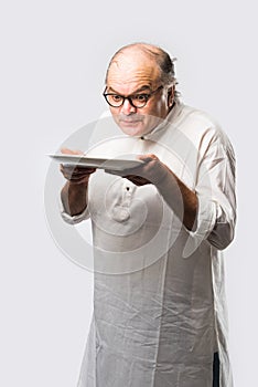 Expressive Indian Old man eating food from empty or blank white plate or bowl