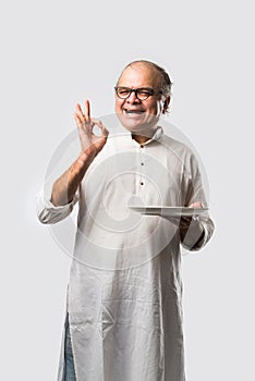 Expressive Indian Old man eating food from empty or blank white plate or bowl