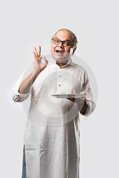 Expressive Indian Old man eating food from empty or blank white plate or bowl