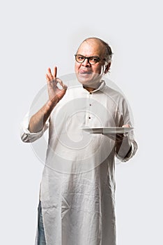 Expressive Indian Old man eating food from empty or blank white plate or bowl