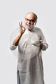 Expressive Indian Old man eating food from empty or blank white plate or bowl