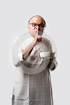 Expressive Indian Old man eating food from empty or blank white plate or bowl