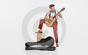 Expressive musician wearing retro style clothes playing guitar like rockstar isolated on white background. Retro style