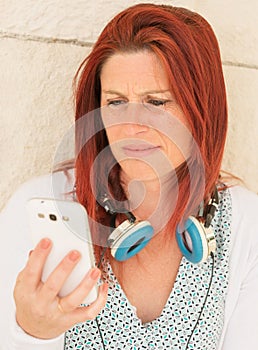 Expressive portrait of a pretty red-haired woman reading the information with annoyance on her mobile phone