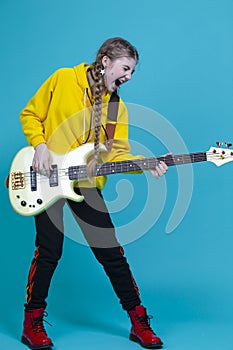 Expressive Positive Caucasian Teenager Guitar Musician Playing On Yellow Bass Guitar Posing In Fashionable Yellow Hoody Jacket