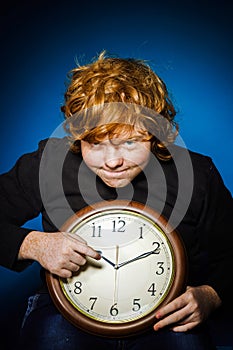 Expressive red-haired teenage boy showing time on big clock