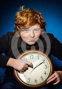 Expressive red-haired teenage boy showing time on big clock