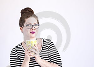 Expressive redhead hugs her coffee cup wearing black glasses and striped top in the studio on a white background