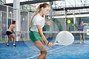 Expressive resolved fit teenage girl playing paddle ball friendly match on small closed court. Concept of competition