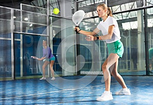 Expressive resolved fit teenage girl playing paddle ball friendly match on small closed court. Concept of competition