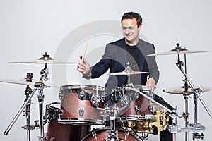 Expressive young drummer playing at the drums with drum stick isolated on white background