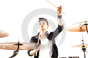 Expressive young drummer playing at the drums with drum stick