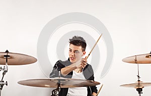 Expressive young drummer playing at the drums with drum stick