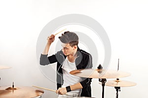 Expressive young drummer playing at the drums with drum stick