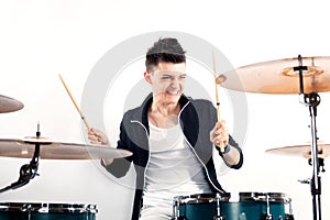Expressive young drummer playing at the drums with drum stick