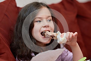 expressive young girl is eating chicken and vegetables for dinner on the couch while watching cartoons