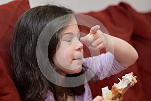 expressive young girl is eating chicken and vegetables for dinner on the couch while watching cartoons