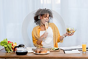 expressive young woman listening music and preparing salad