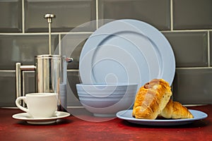 expresso coffee cup and saucer stainless steel cafetiere with fresh coissant blue dinner set on red linoleum work top with grey