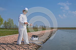 Exquisite fishing. Fisherman in white suit catch fish by spinning rod at trout area lake