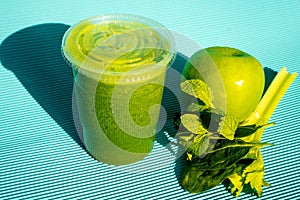 Exquisite green apple juice with mint  inside a plastic cup with a green apple and mint on the side on a blue table