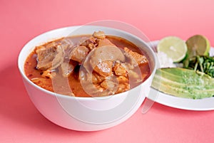 Exquisite Mexican Menudo on a white plate accompanied by a dish with condiments on the back photo