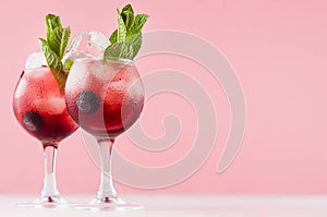 Exquisite red alcoholic shots of sweet berry liquor with ice cubes, blueberry, green mint on pastel soft light pink background.