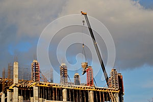 An extended boom of a truck crane lifts a concrete tank to the top floor of a building under construction.