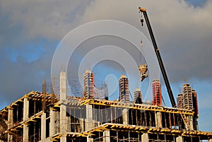 An extended boom of a truck crane lifts a concrete tank to the top floor of a building under construction.