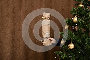 Extended children`s hand with a New Year`s flap surprise. From behind a loaded Christmas tree.