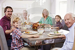 Extended Family Group Sit Around Table Eating Meal At Home