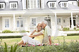 Extended Family Group Sitting Outside House On Lawn