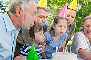 Extended family in party hats blowing birthday cake