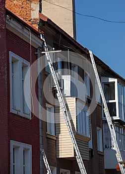 An extension ladder leans against the front of a multifamily housing building in preparation of roof repairs