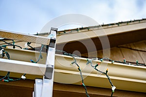 extension step ladder against side of roof with a strand of Christmas lights