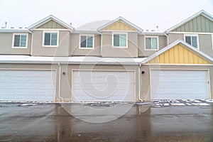 Exterior of apartments with white garage doors along wet snowy road in winter