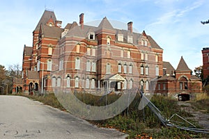 Exterior of boarded up and abandoned brick asylum hospital building with broken windows