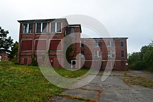 Exterior of boarded up and abandoned brick asylum hospital building with broken windows