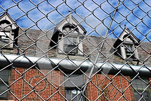 Exterior of boarded up and abandoned brick asylum hospital building with broken windows surrounded by chain link fence