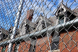 Exterior of boarded up and abandoned brick asylum hospital building with broken windows surrounded by chain link fence