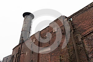 Exterior brick wall of an industrial facility with deeply weathered smokestack, gray sky winter