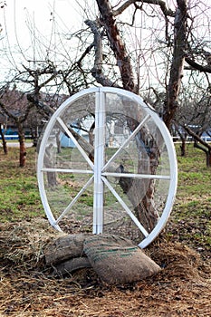 Exterior decor of wedding ceremony in a rustic style. Large wooden wheel with bags and hay next  trees in the garden. Beautiful ga