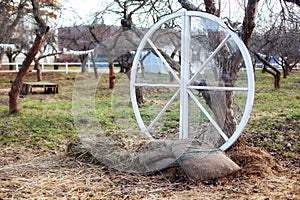 Exterior decor of wedding ceremony in a rustic style. Large wooden wheel with bags and hay next  trees in the garden. Beautiful ga