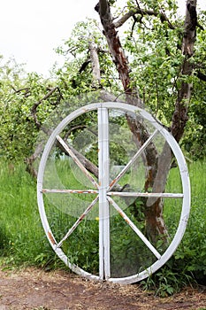 Exterior decor of wedding ceremony in a rustic style. Large wooden wheel with bags and hay next  trees in the garden. Beautiful su
