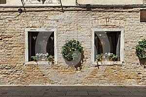 Exterior detail a window with a metal grille and red flowers in a pot in Venice, Italy