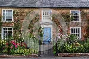 The exterior of an english cottage with flowers blooming in the front garden and sash windows, A typical english countryside