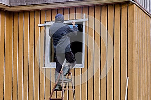 Exterior finishing of plastic window in frame-panel wooden country house, construction worker installs metal slopes